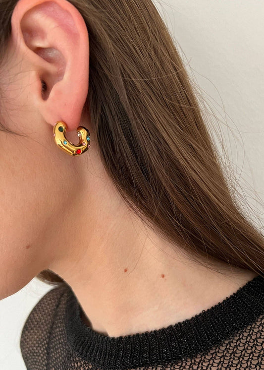 Close-up of a person wearing a gold earring with colorful stones.