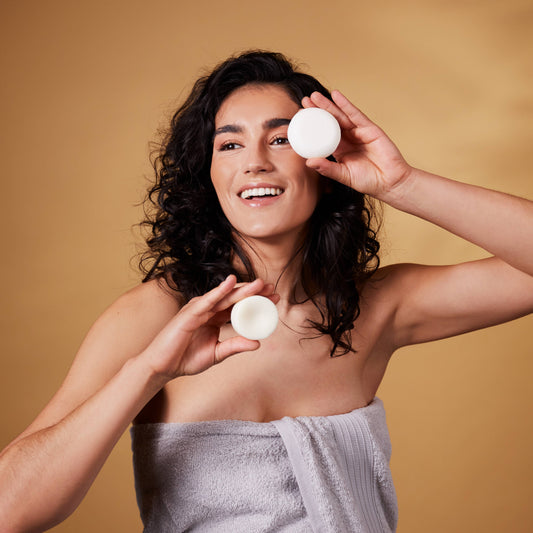 Woman holding two zero waste shampoo and conditioner bars against a beige background