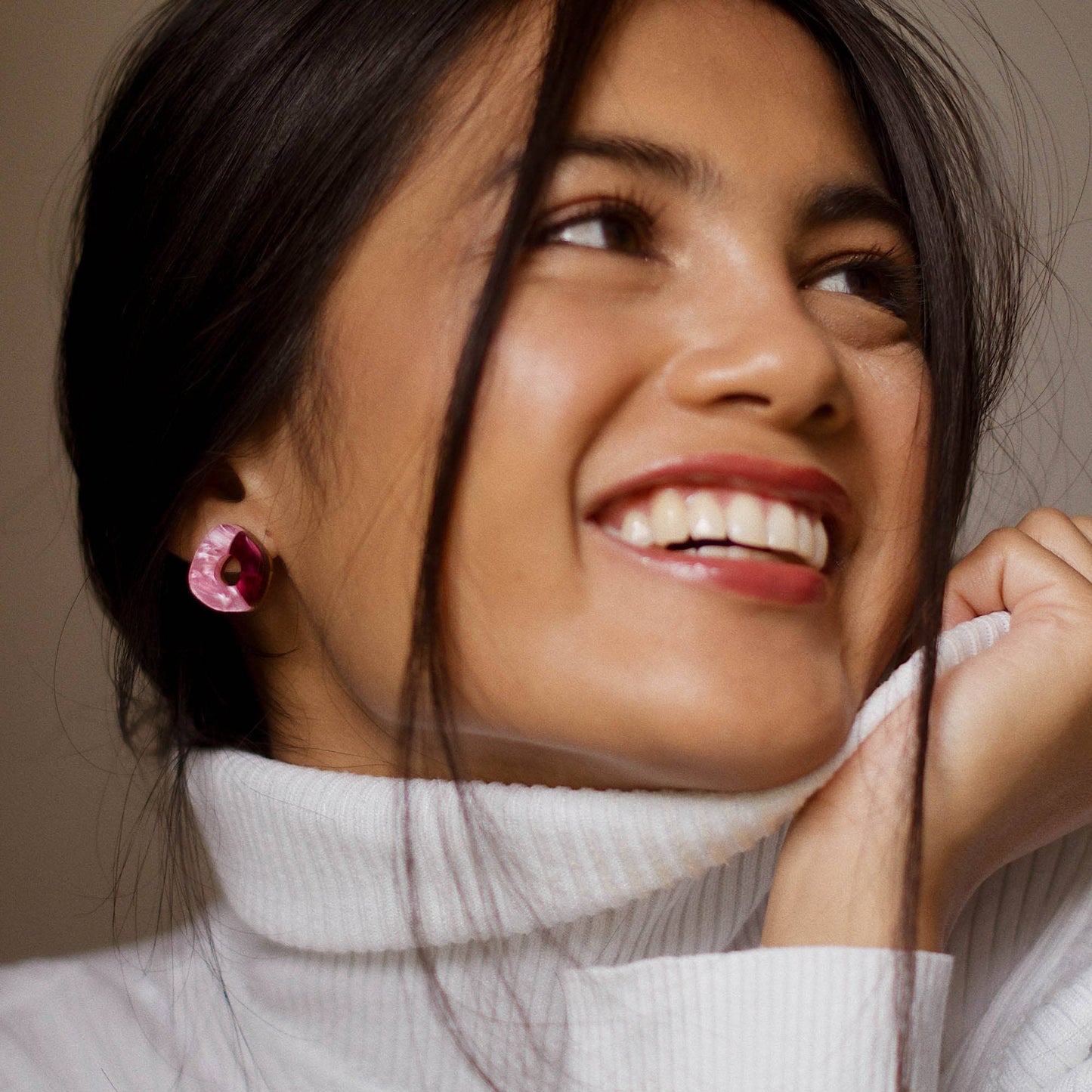 Woman wearing pink and berry earrings with a neutral background