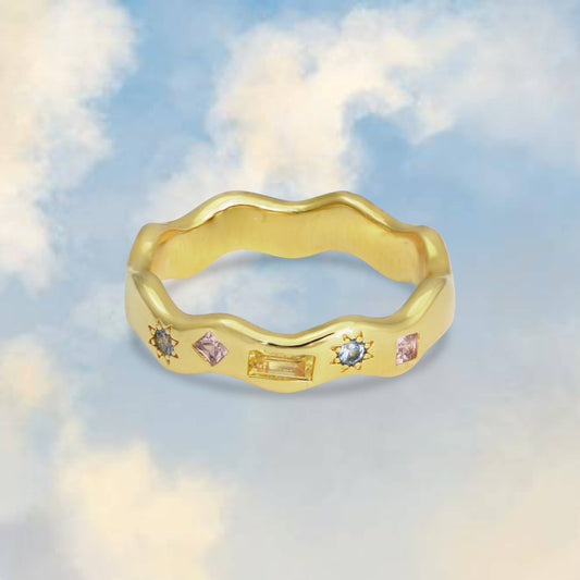 Gold ring with embedded gemstones against a cloudy sky background