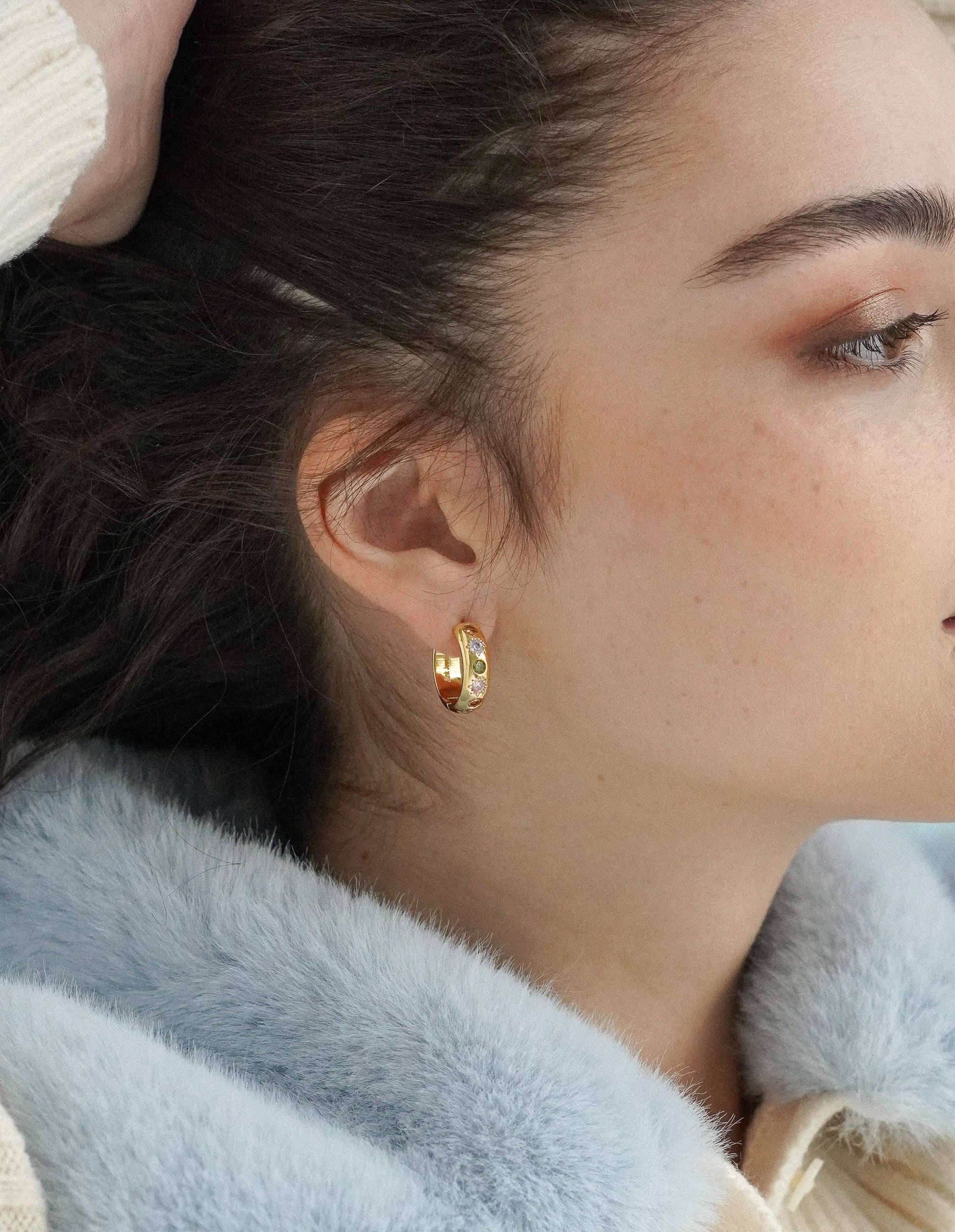 Close-up of a person wearing gold hoop earrings with a soft focus on the face and hair.