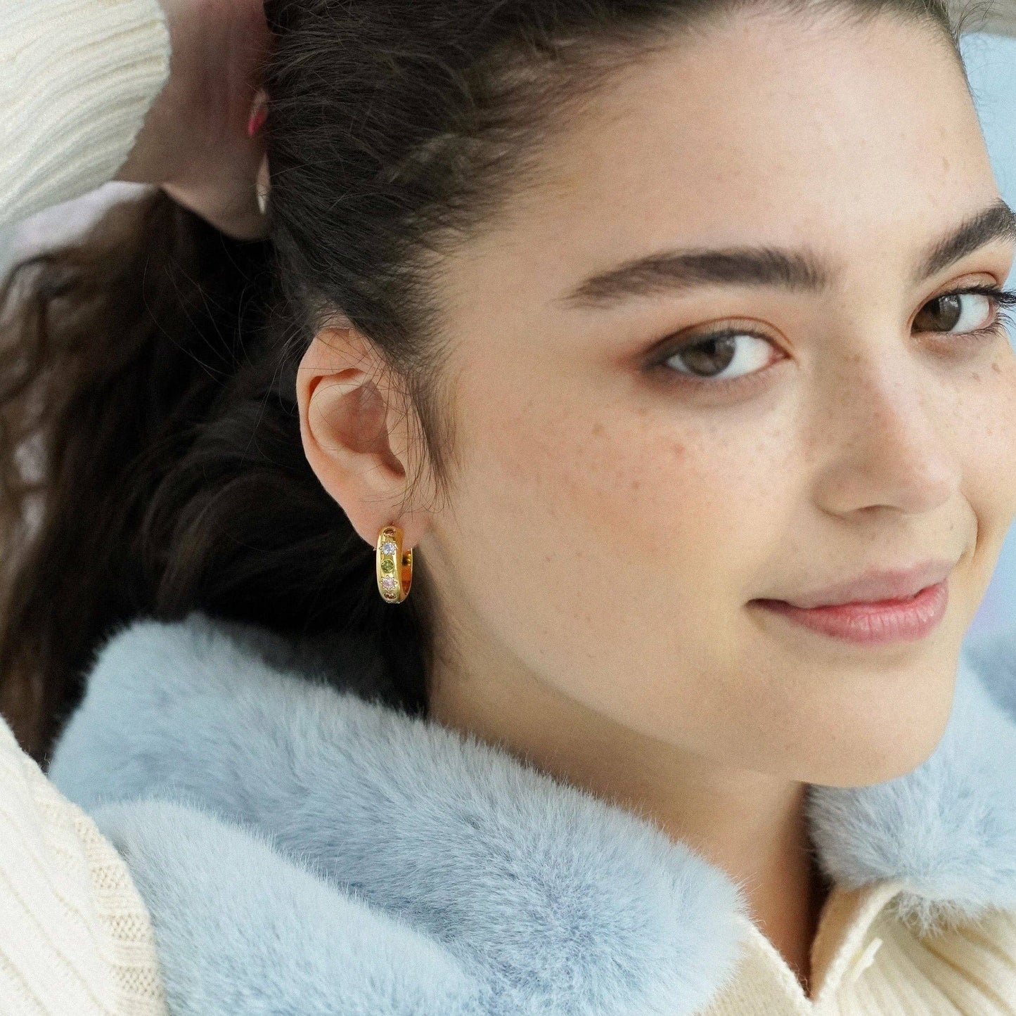 Close-up of a woman wearing colorful hoop earrings with a light blue fur collar.