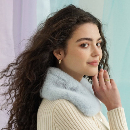 Woman wearing a light-colored sweater and light blue scarf against a pastel background