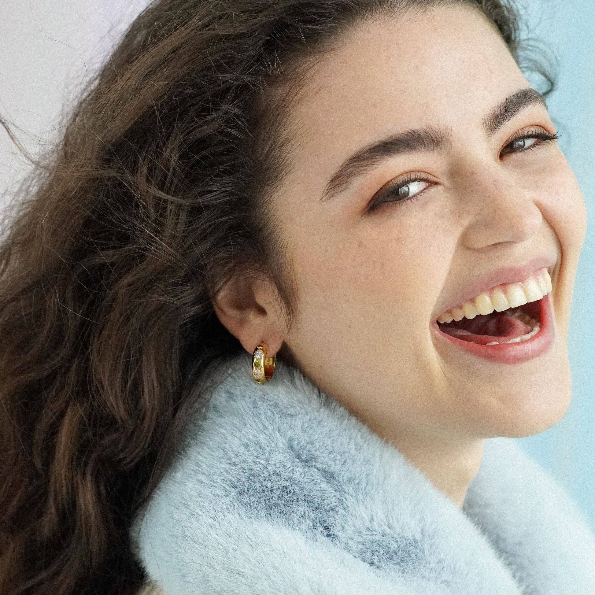 Woman with a bright smile wearing gold earrings against a light background