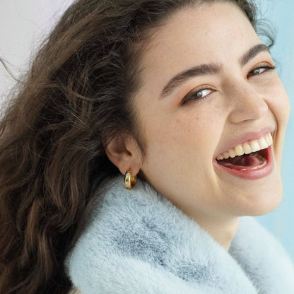 Woman with a bright smile wearing gold earrings against a light background