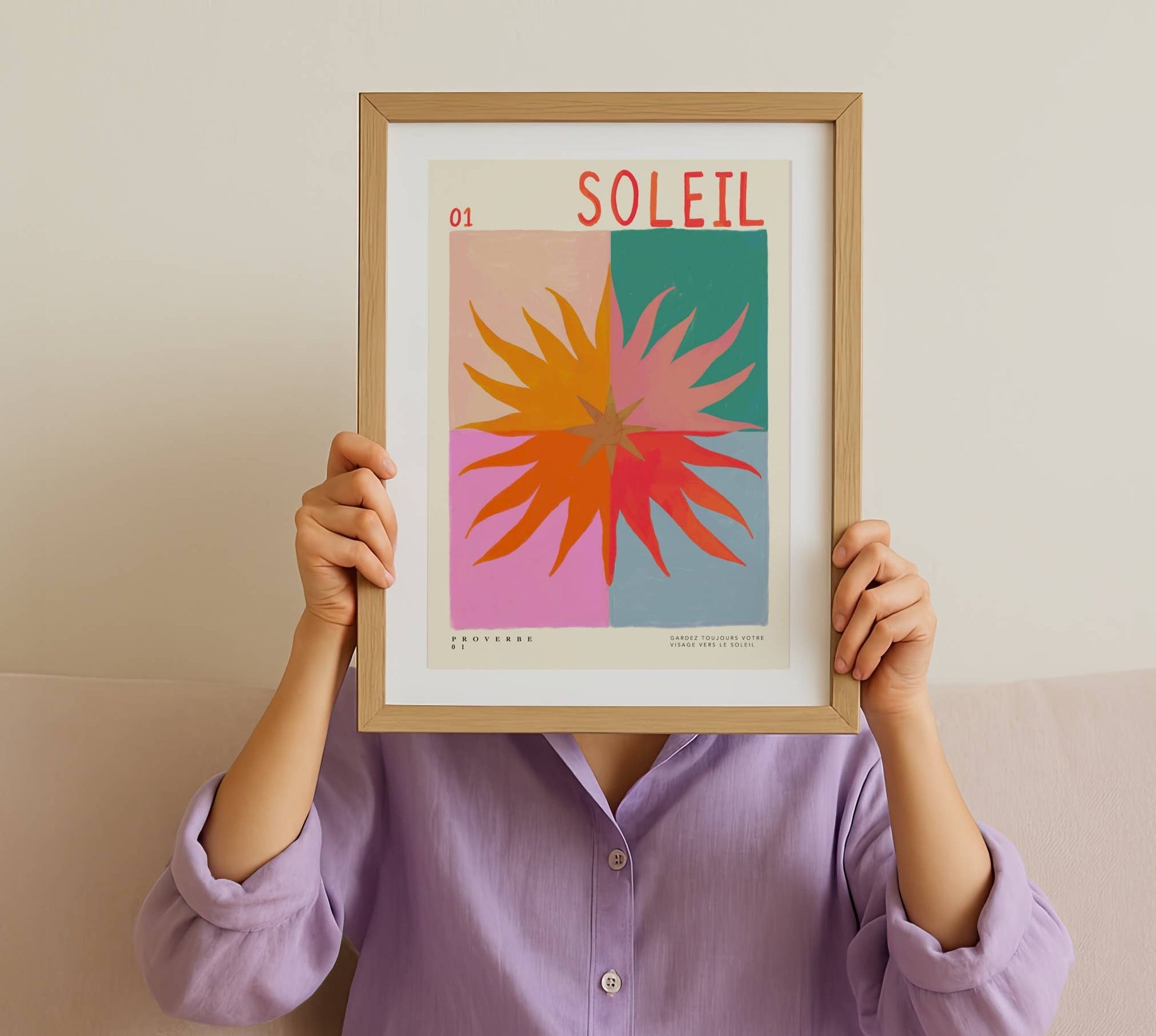 Person holding a framed colorful print with 'Soleil' and a sun design.