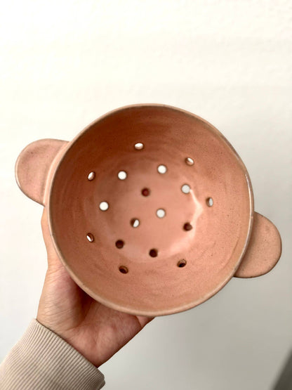 Ceramic colander with bear ears held by a hand against a neutral background