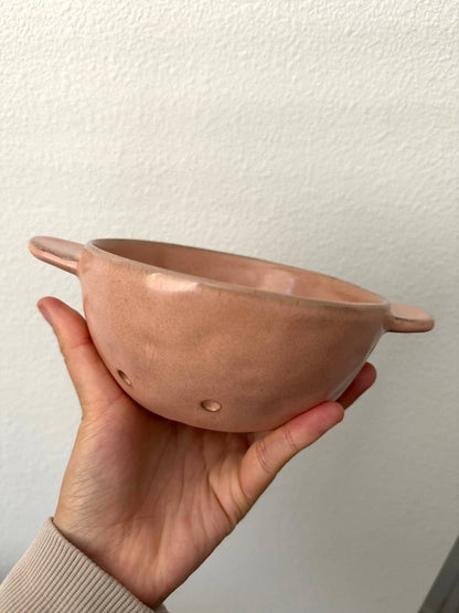 Hand holding a pink ceramic bowl against a plain background