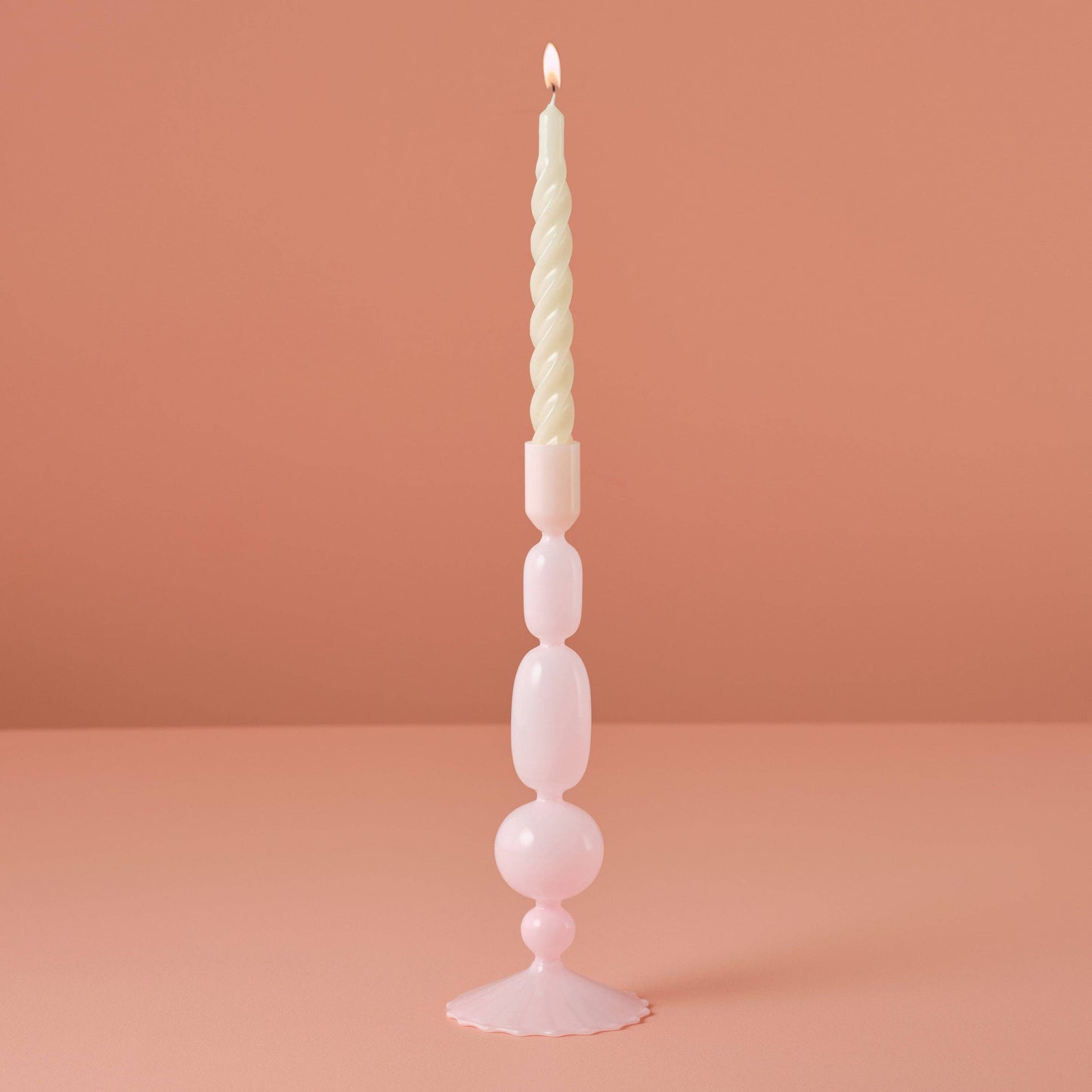 Tall, decorative candle with a unique design on a pink background