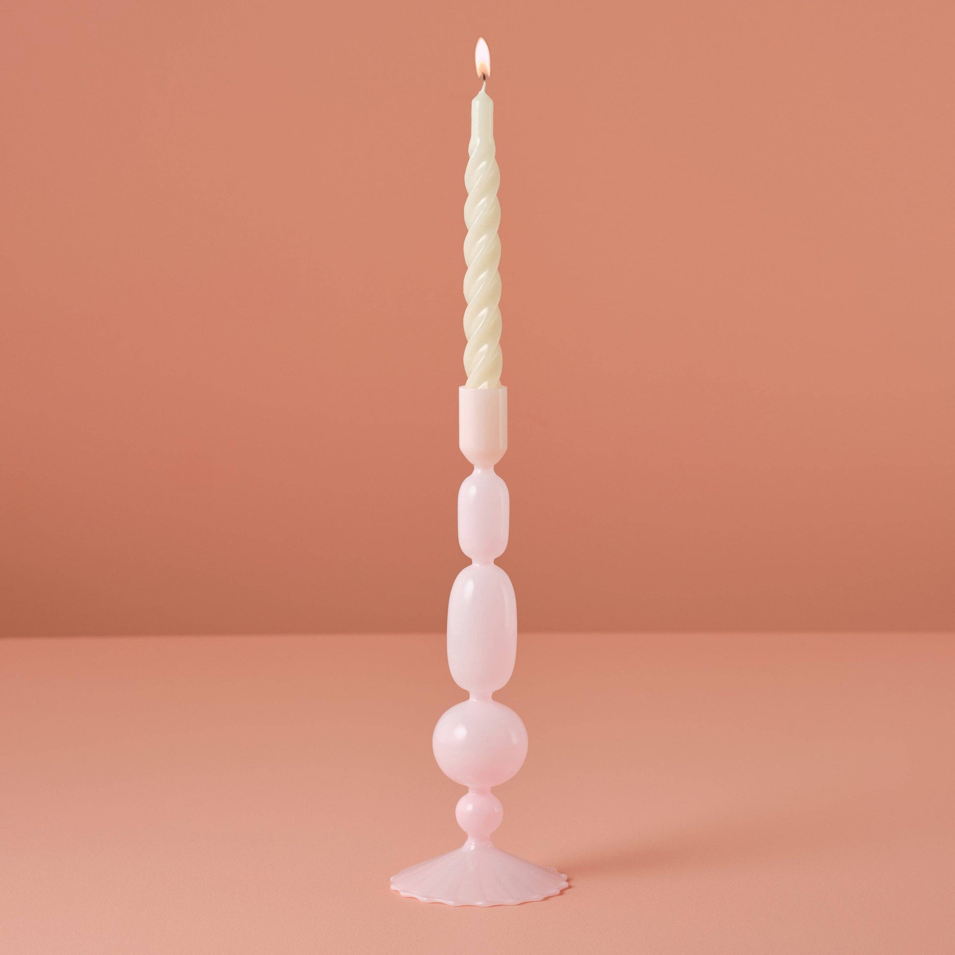 Tall, decorative candle with a unique design on a pink background