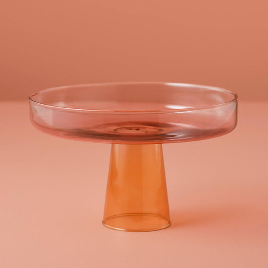 Clear glass cake stand on a peach-colored background