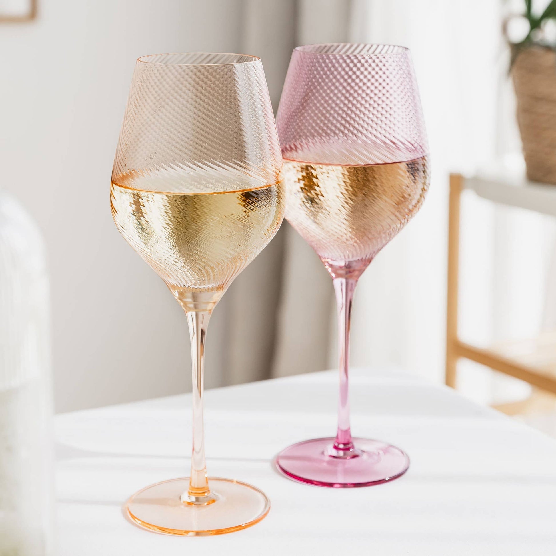 Two textured wine glasses filled with white wine on a light surface.