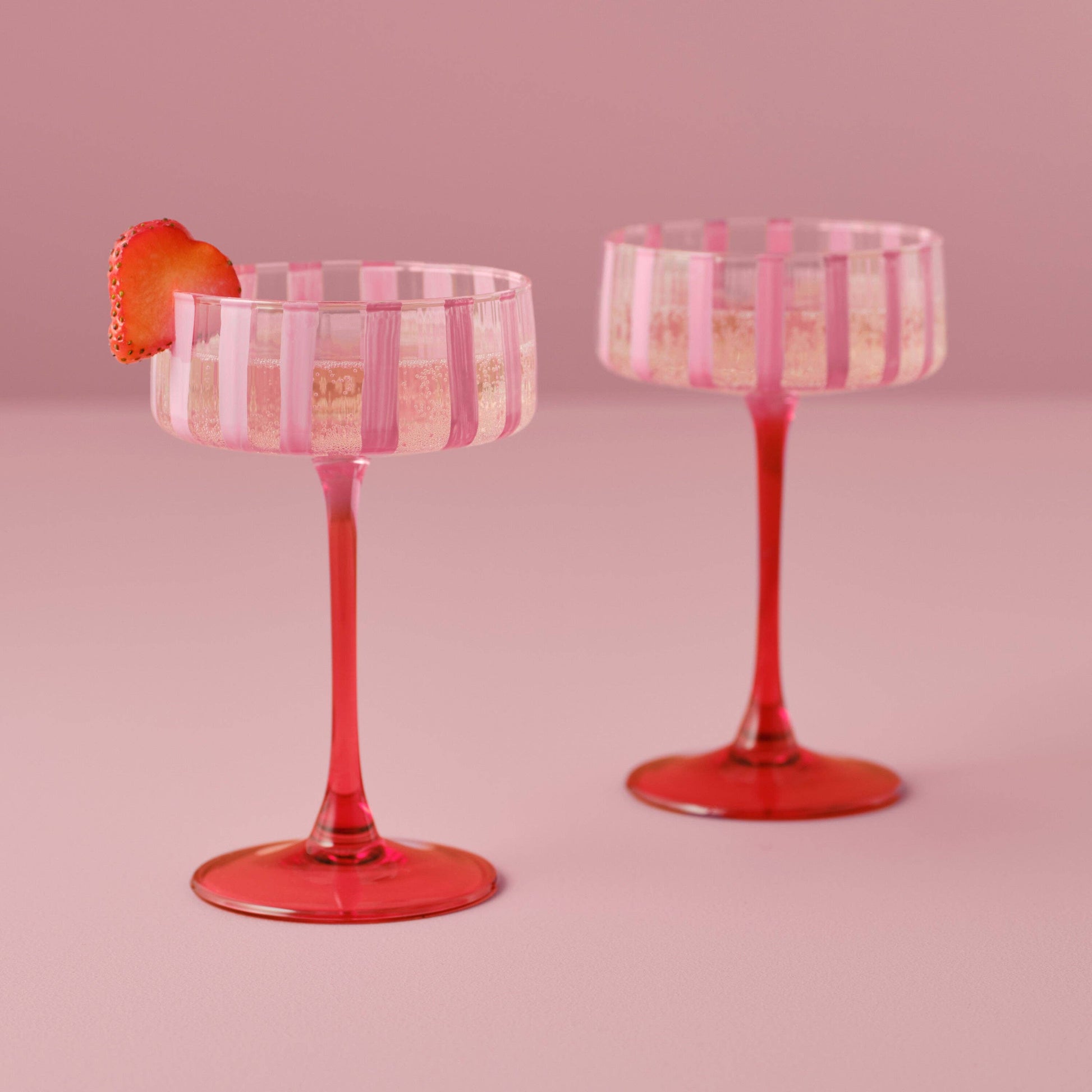 Two pink and red striped cocktail glasses on a pink background