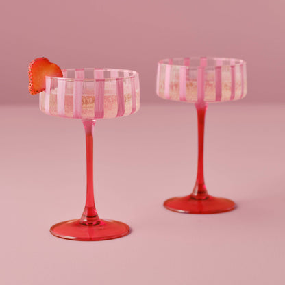 Two pink and red striped cocktail glasses on a pink background