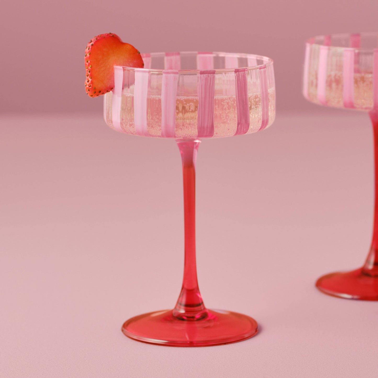 Pink striped cocktail glass with a strawberry on a pink background