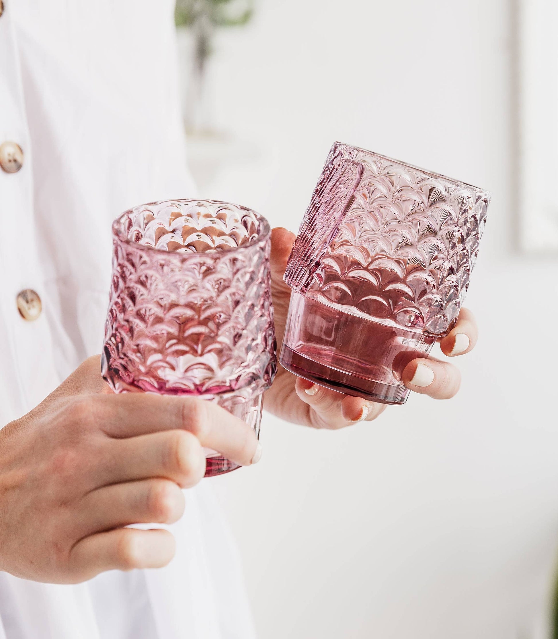 Two pink textured glass tumblers held by a person against a white background