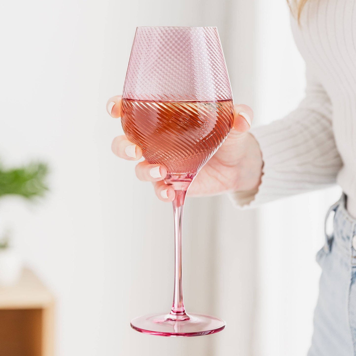 Pink wine glass held by a person with a blurred background