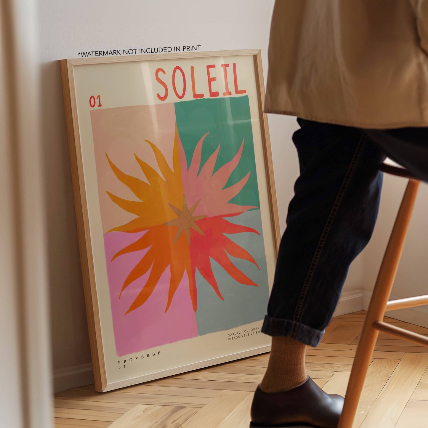 Poster with 'Soleil' design leaning against a wall next to a person sitting on a stool.