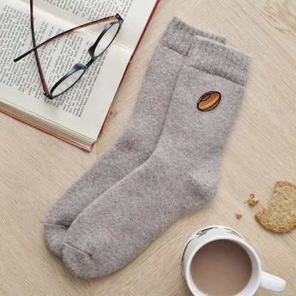 Gray socks with a coffee bean design on a wooden surface with a book, glasses, and cookies.
