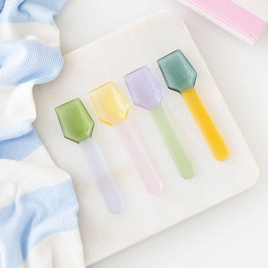 Set of colorful ice cream spoons on a white surface with a striped fabric background.