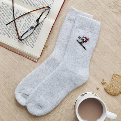 Gray socks with a small embroidered design on a wooden surface with a book, glasses, and a mug.