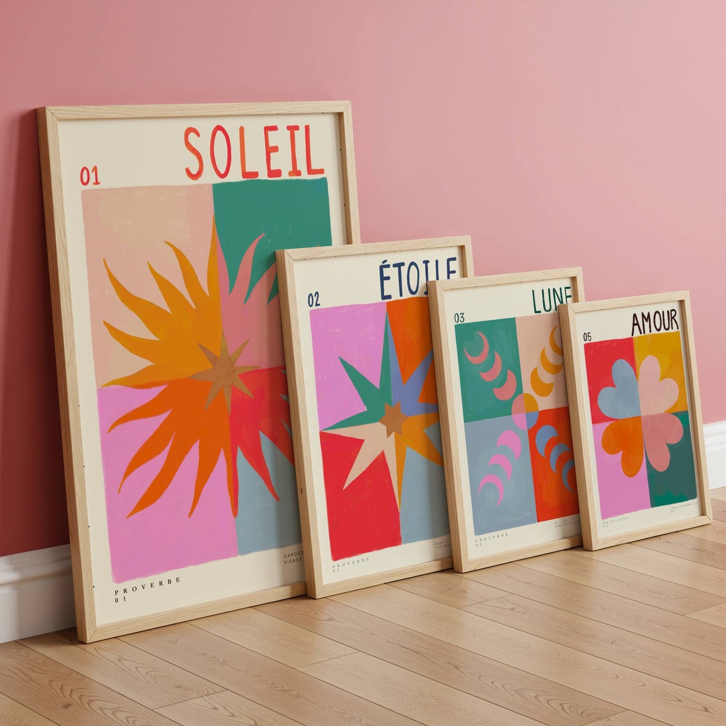 Four colorful framed artworks on a wooden floor against a pink wall.
