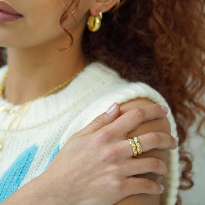 Close-up of a person wearing gold earrings and a gold ring, with a blurred background.