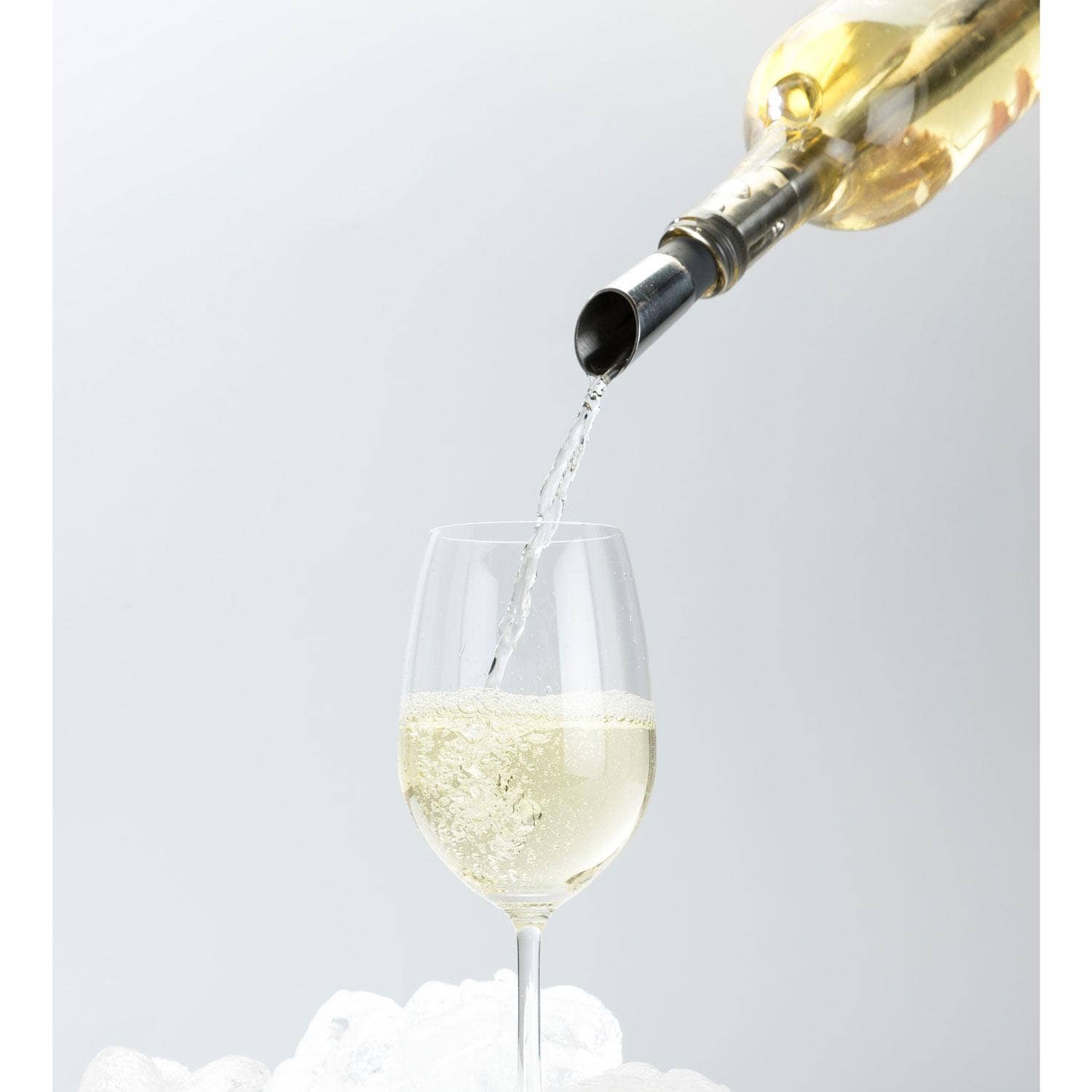 White wine being poured from a bottle into a glass against a light gray background
