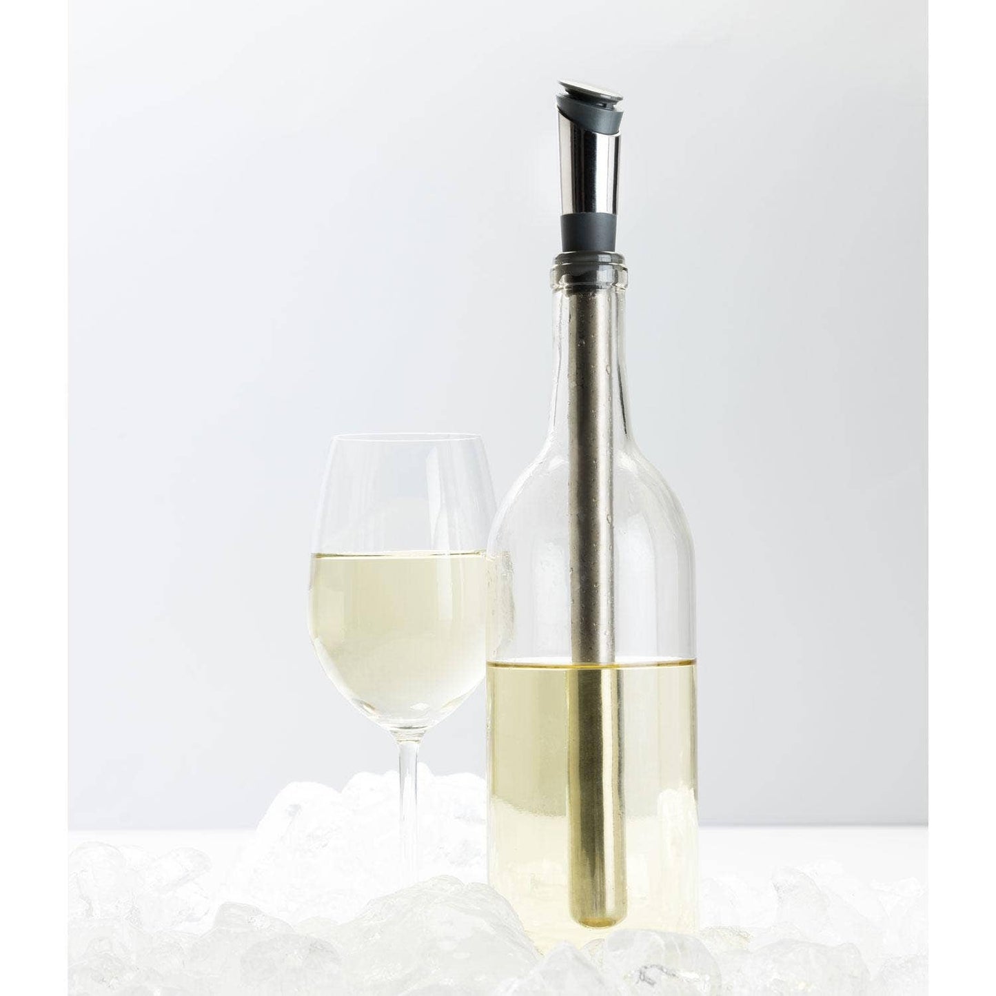 Clear wine bottle with gold foil top and a glass of white wine on a light gray background