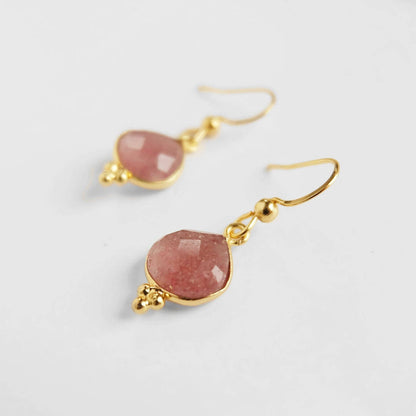 Gold earrings with pink stones on a light gray background