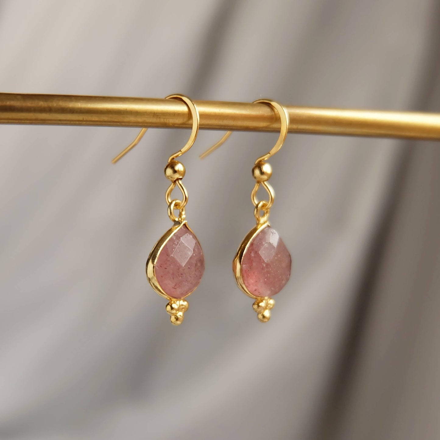 Gold earrings with pink stones on a gold rod against a gray background