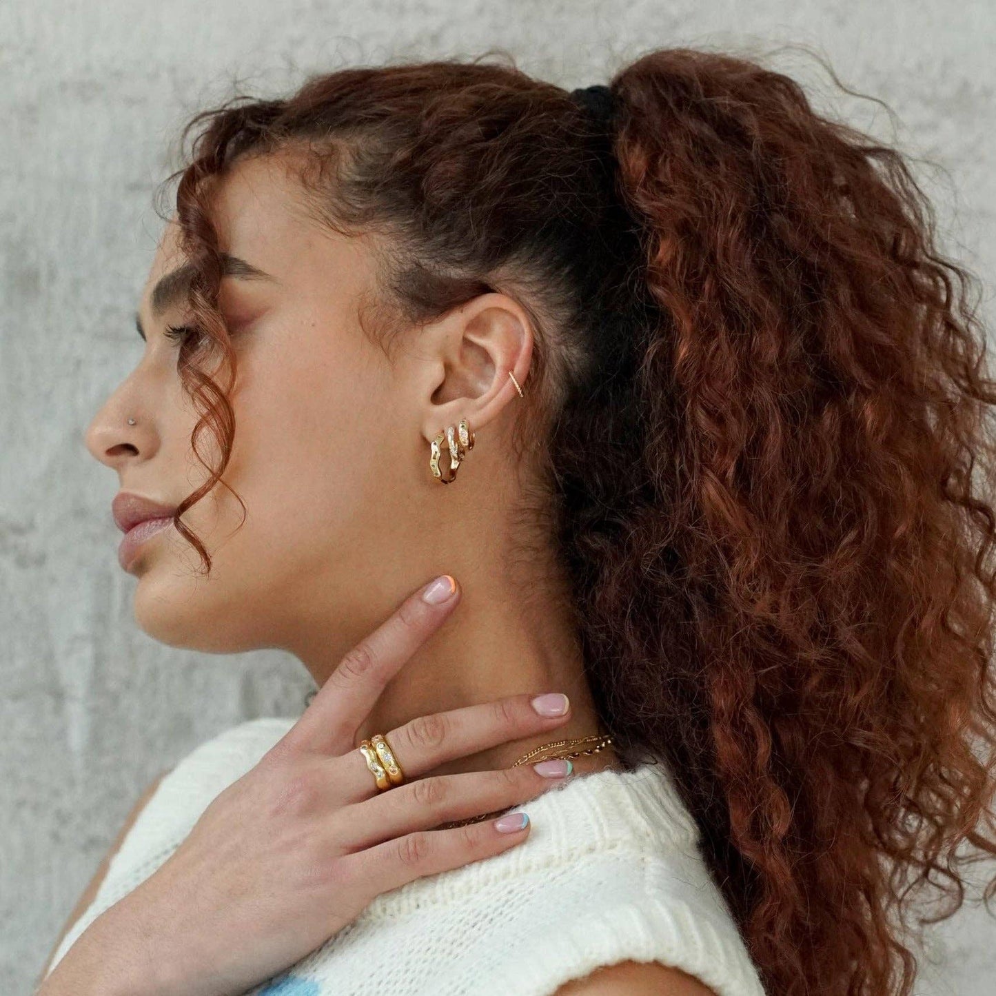 Woman with styled hair and jewelry against a neutral background