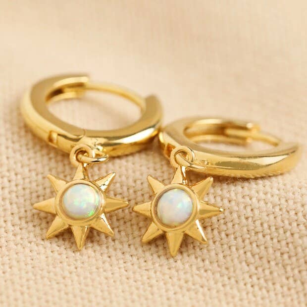 Gold hoop earrings with star-shaped charms on a beige fabric background