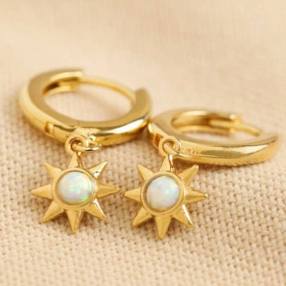 Gold hoop earrings with star-shaped charms on a beige fabric background
