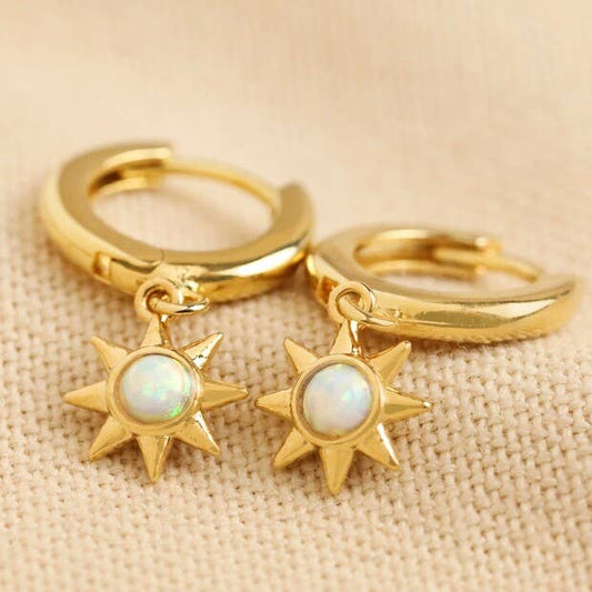 Gold hoop earrings with star-shaped charms on a beige fabric background