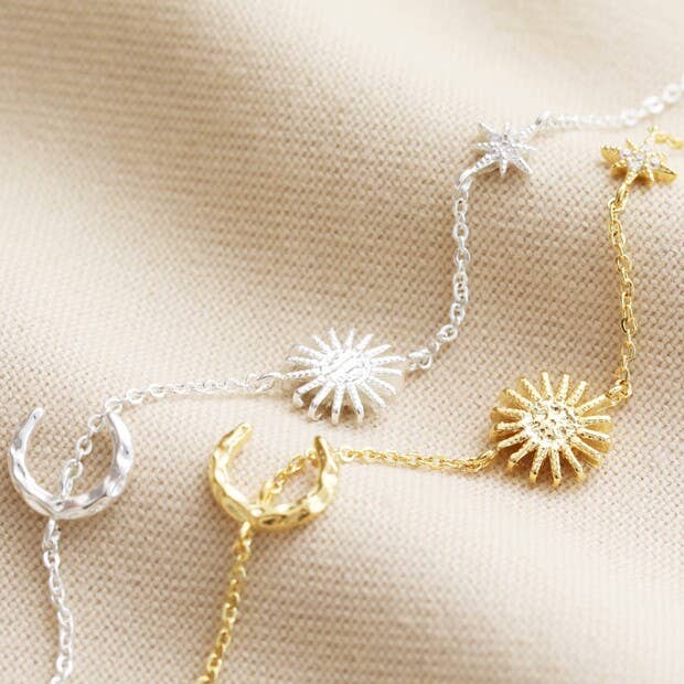 Two delicate necklaces with sun and moon designs on a beige fabric background