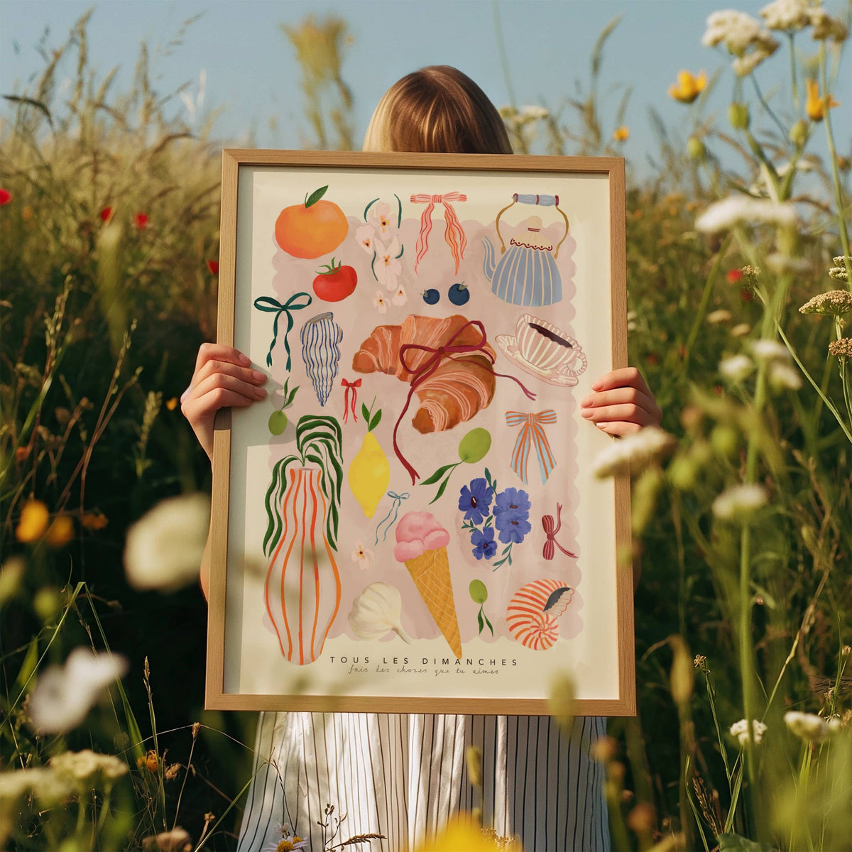 Person holding a framed illustration in a field of flowers