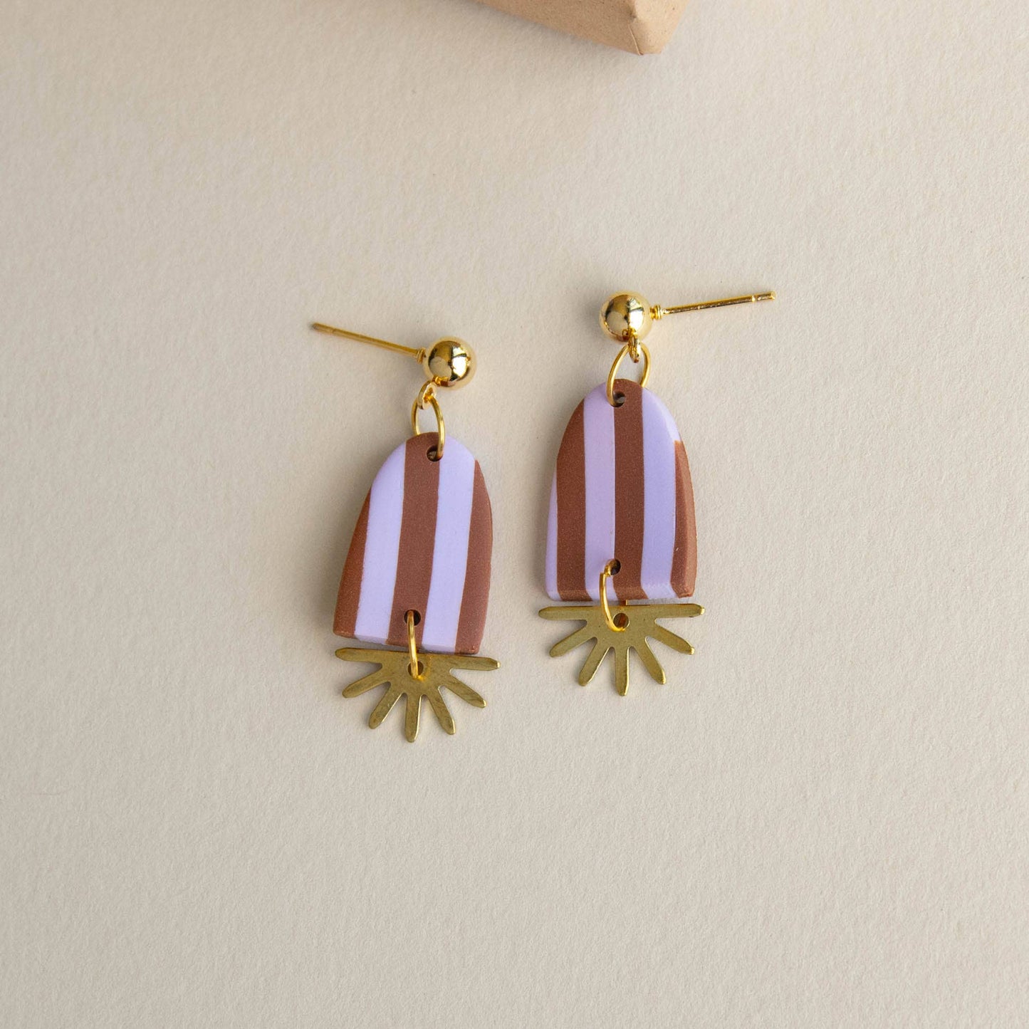 Pair of earrings with striped design and gold accents on a beige background