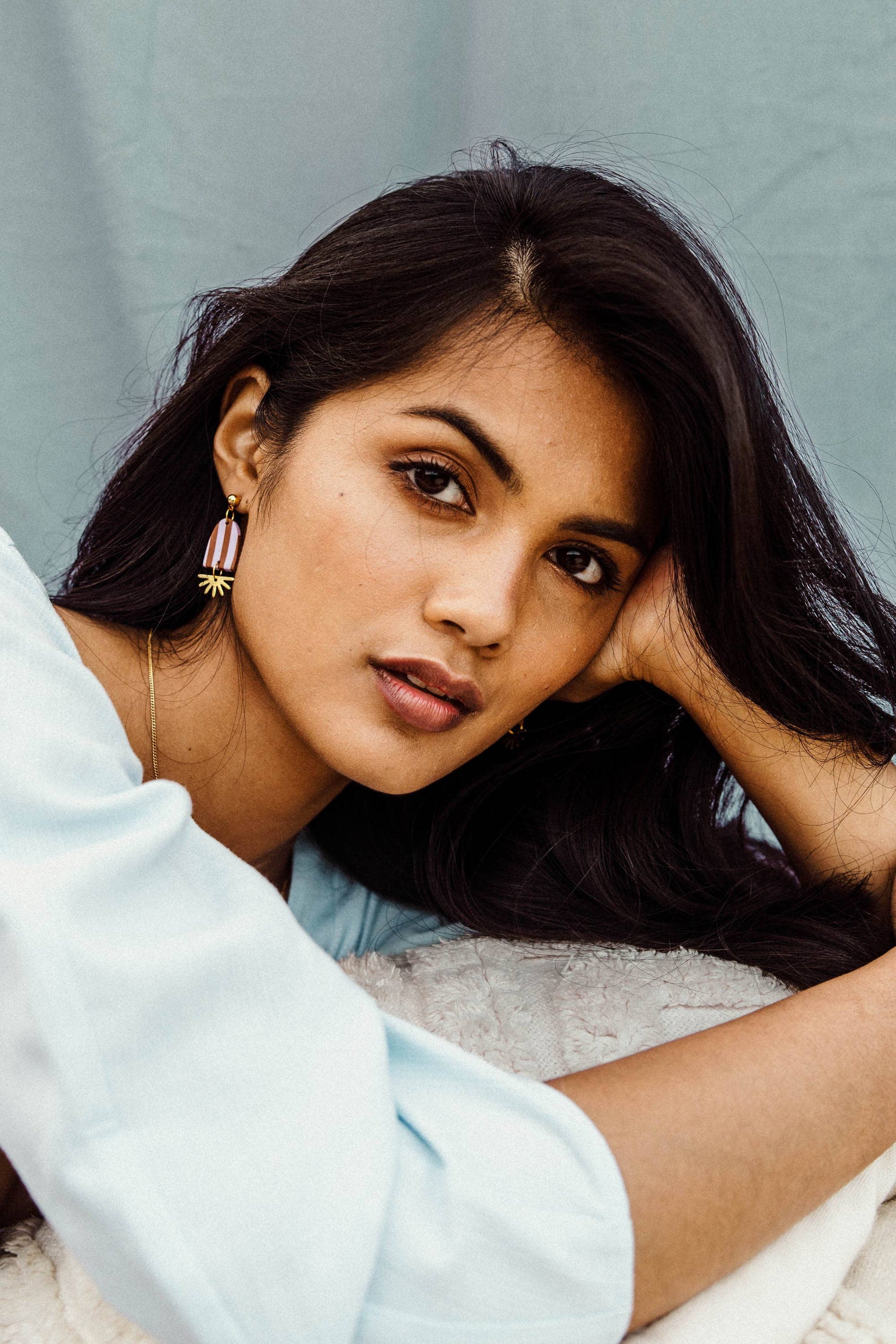 Woman with dark hair and earrings, wearing a light blue shirt against a neutral background