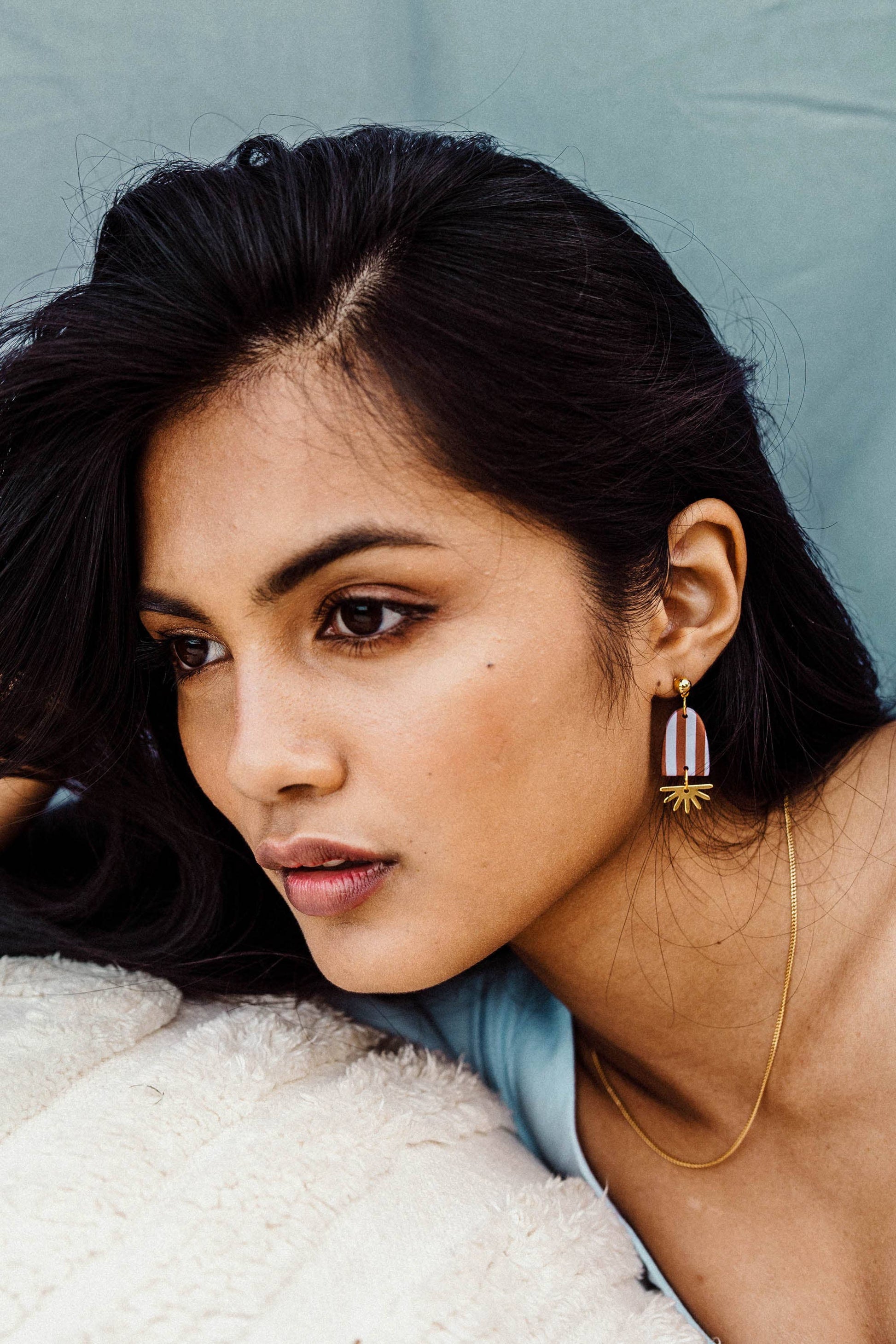 Woman wearing earrings and a necklace against a neutral background
