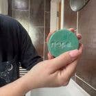 Person holding a round green object with text against a blurred bathroom background