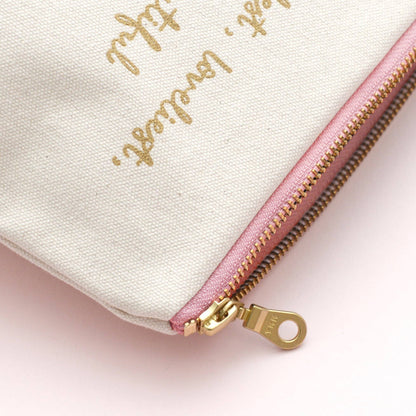 Close-up of a beige pouch with gold text and a pink zipper on a light pink background