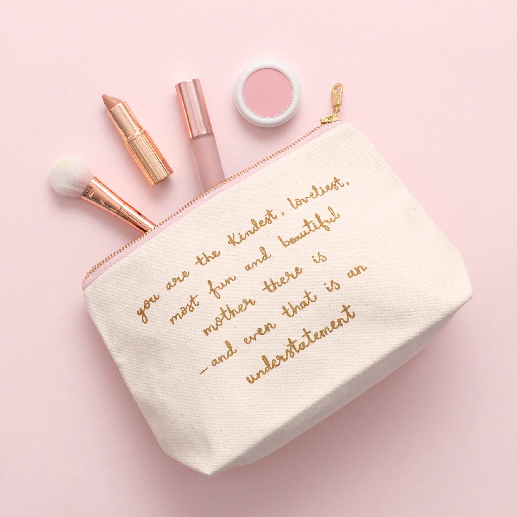 Cosmetic bag with gold text, lipsticks, and makeup brushes on a pink background