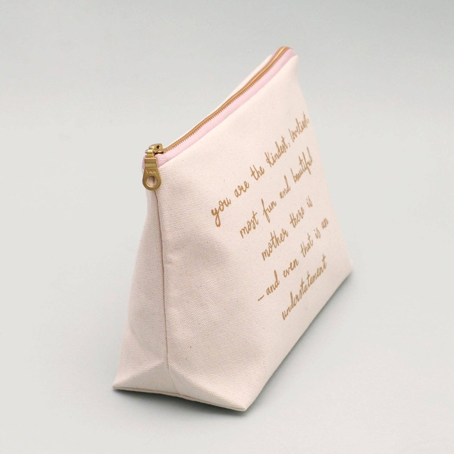 Cream make up pouch with gold text on a light gray background