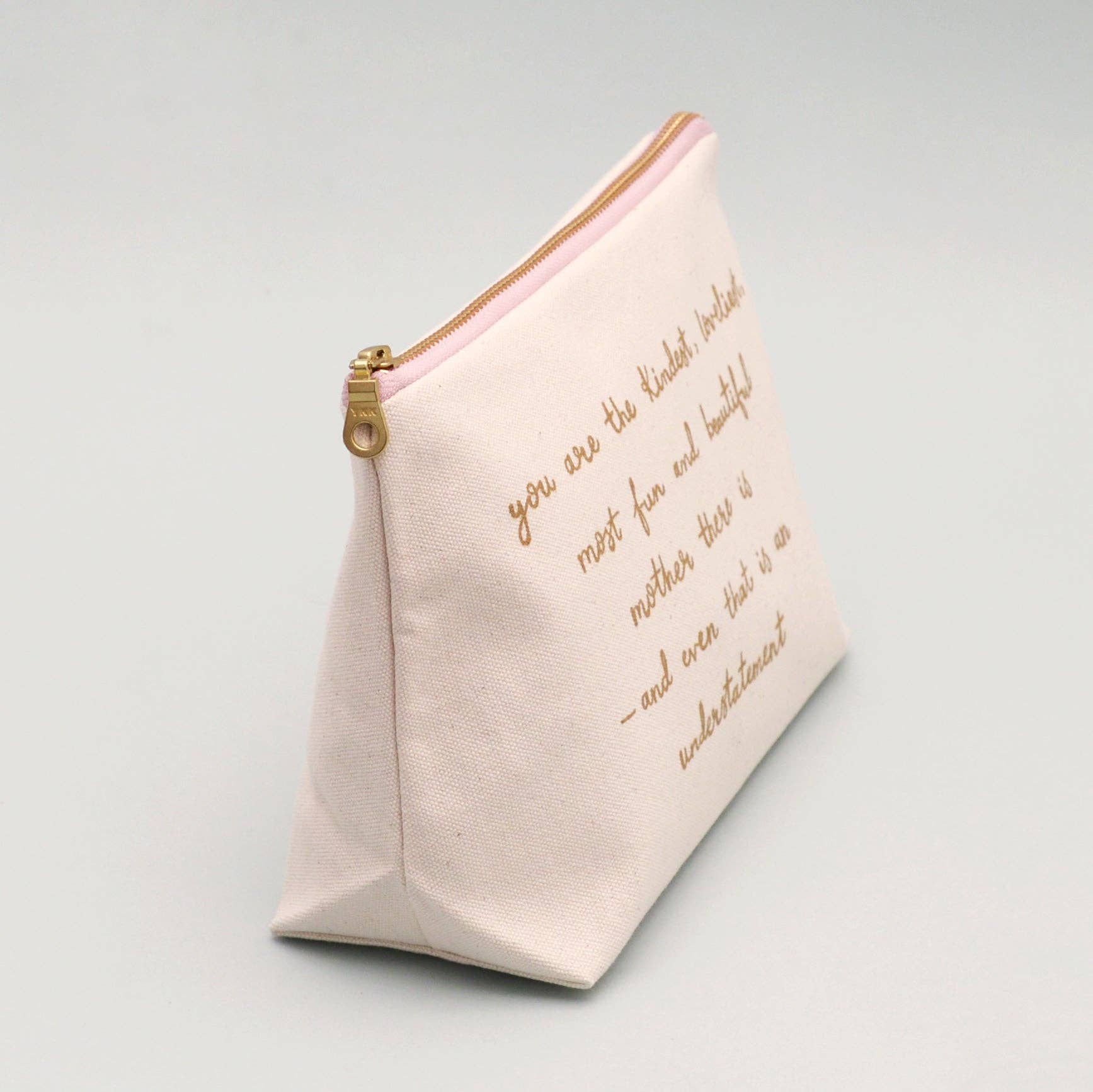 Cream make up pouch with gold text on a light gray background