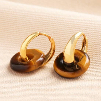 Gold hoop earrings with brown gemstones on a beige fabric background