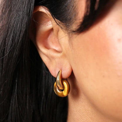 Close-up of a person wearing a gold hoop earring with dark hair.