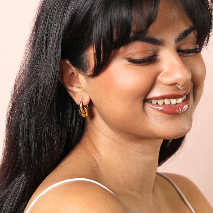 Woman wearing gold hoop earrings with a soft pink background