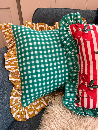 Turquoise gingham cushion with yellow chain frill next to cherry striped cushion with turquoise frill