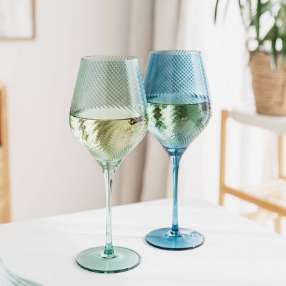 Two textured wine glasses filled with white wine on a light surface.